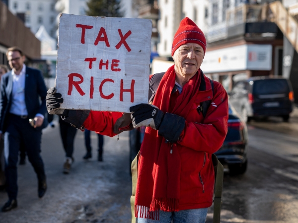 O megaempresário britânico Phil White segura um cartaz onde se lê: &#039;Taxe os ricos&#039; durante o Fórum Econômico Mundial. Mais de 200 milionários em 13 países defendem maior tributação para quem ganha mais. No Brasil, as elites acusam a medida de ser uma prática “socialista”